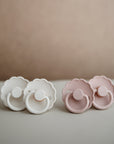 Two Cream and two Blush Frigg Daisy baby pacifiers on a neutral background