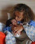 A young girl holding a baby with a Frigg Moon Rubber pacifier in bed.