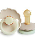 Two Frigg Daisy Night Rubber baby pacifiers in Cream and Croissant on a white background