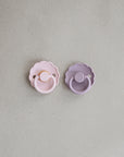 Two pacifiers, one Baby Pink and one Soft Lilac, on a light gray background