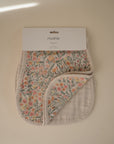 A mushie Organic Cotton Muslin Burp Cloth from the 2-Pack is shown with a corner folded to reveal its soft inner layer, featuring a floral pattern and set against a plain beige background.