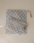 The mushie Water Resistant Wet Bag set includes two checkered pouches—one large with a wrist strap and one small—featuring blue and white squares, beige zippers, and ideal for diaper bag storage.