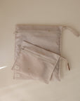 Two mushie Water Resistant Wet Bags, one large and one small in pale pink with star patterns, rest on a beige surface. Each pouch has a fabric pull tab and white tag—ideal for diaper bag storage.
