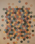 A mosaic of interlocking, flower-shaped pieces from the mushie HEX Connect Building Toy Set in assorted colors forms a rectangular pattern, with extra pieces scattered along the edges on a plain surface.