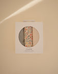 A box of Mushie Changing Pad Liners is shown against a beige background. Made from organic cotton, the light-colored liners include one with a floral pattern visible through a circular cutout in the packaging.