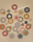 The mushie Foam Bath Puzzle features colorful foam cutouts—circles, hearts, stars, hexagons, and squares—that add playful charm and highlight educational benefits when arranged on a neutral background.