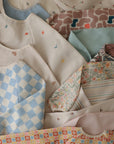 The mushie Long Sleeve Bib collection features water-resistant bibs with neat designs in pastel florals, stripes, checks, rainbows, birds, and abstract shapes.