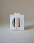 A boxed set of three Mushie Changing Pad Liners made from folded organic cotton muslin in green, pink, and beige pastel tones, displayed inside white packaging with a circular window on a plain beige background.
