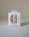 A white Mushie box with a circular window displays two Changing Pad Liners—one in beige and dusty pink checkerboard, the other solid beige—against a light background. Both are made from organic cotton muslin.