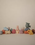 A row of mushie Vehicles Mold Free Bath Play Set silicone bath toys—featuring minimalistic, soft, pastel-colored vehicles—arranged against a plain beige background. These smooth toys are mold-free for safe and stylish bath time fun.