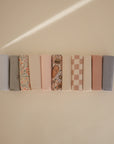 Ten Mushie Changing Pad Liners are neatly arranged side by side on a beige surface, displaying florals, checks, and solid colors in soft pastel and neutral tones.