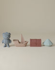 Lifestyle images of a set of Mushie's silicone Pirate Bath Play Set, including a bear, boat, a diamond, and treasure chest on a beige background
