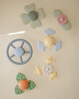 The mushie Suction Spinner Toy features pastel-colored silicone shapes like flowers, steering wheels, turtles, clouds, and leaves. Soft and rounded, these toys offer young children a fun sensory play and exploration experience.