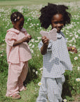 Two kids in gingham pick flowers; one holds a mushie Silicone Sensory Toy shaped like a butterfly.