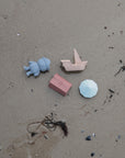 Lifestyle image of the mushie Pirate Bath Play Set toy son a sandy ground.