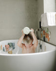 A child enjoys sensory fun in the tub with the mushie Pour and Play Bath Set.