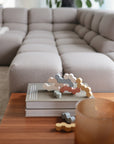 A close-up of a modern living room featuring a light grey tufted sectional sofa, wooden coffee table, and mushie Wooden Balance Blocks—abstract pastel stacking toys crafted from FSC-certified wood—with a translucent brown glass.