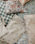 A selection of mushie Water Resistant Wet Bags, featuring floral, checkered, rainbow, and leaf patterns in pastel colors, is neatly arranged on a flat surface. These bags are ideal for diaper bag storage and keeping items dry.
