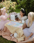 Three young girls in white dresses sitting on a blanket outdoors with pumpkins and a map.