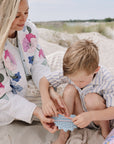 Woman and child on sand, smiling at mushie Silicone Sensory Toy.