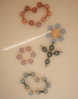 Four pastel flower-shaped creations, made from interlocking plastic pieces in pink, blue, and yellow, are arranged on a light surface. Built using the mushie HEX Connect Building Toy Set, they feature circular and floral patterns.