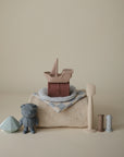 Lifestyle image of mushie bath items, including a cotton Fog hooded towel, the silicone Pirate Bath Play Set, a silicone Shifting Sand diaper applicator and silicone bear and dog Animal Finger Puppets on a neutral background.