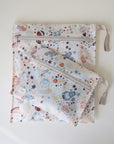 The mushie Water Resistant Wet Bag set includes two zippered pouches with beige handles and a vibrant space-themed design. Ideal for diaper bag storage, the smaller pouch overlaps the larger one for convenient organization.