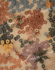 A close-up of the mushie HEX Connect Building Toy Set shows pink, blue, brown, purple, and beige interlocking pieces overlapping on a cream surface. Some are joined as flowers, inspiring spatial reasoning through creative play.