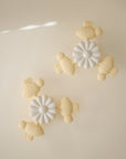 Four pastel yellow mushie Suction Spinner Toys shaped like turtles and two white daisy spinners are symmetrically arranged on a beige background, forming a playful, minimalist pattern that invites a fun sensory experience.