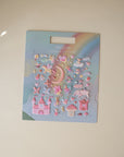 The mushie Reusable Sticker Set features pastel moon, stars, unicorns, castles, and hearts on a rainbow background. Shown on a light surface—great for fans of reusable or puffy stickers. Packaging reads "mushie Reusable Sticker Set.