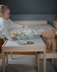 A young child hosts a pretend tea party with a teddy bear, playfully pouring from a toy teapot as the FRIGG Butterfly Anatomical Silicone Pacifier 2-Pack (0-6 Months) by FRIGG rests nearby in the softly lit room.