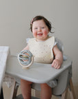 Child in a high chair with a suction spinner ball toy, sitting on a neutral background