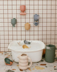 Mushie Pour and Play Bath Set: toy whales and cups for sensory fun by the bath basin.