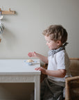 A young child sits at a small white table, reaching for mushie Suction Spinner Toys made of food-grade silicone. A hot air balloon ornament decorates the softly lit room, creating a gentle sensory experience.
