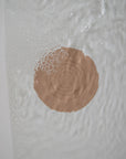 A round, flesh-toned mushie Silicone Drain Stopper with concentric circles rests underwater amid ripples and bubbles, echoing its function as an innovative bath accessory.