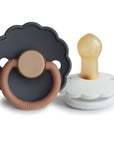 The FRIGG Daisy Natural Rubber Pacifier 2-Pack includes two daisy-shaped pacifiers—one dark gray with a tan handle, one white with a tan natural rubber nipple—both featuring the FRIGG brand on the front.
