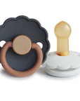 The FRIGG Daisy Natural Rubber Pacifier 2-Pack includes two scalloped-edge pacifiers: one in dark gray with a brown handle and one in white with a tan natural rubber latex nipple.