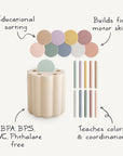 The mushie Coin & Tube Sorting Set features a beige container, pastel coin-like pieces, and matching sticks. This non-toxic educational toy promotes color recognition, fine motor skills, and sorting practice.
