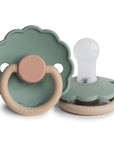 The FRIGG Daisy Silicone Pacifier 2-Pack | Limited Edition features two flower-shaped pacifiers in sage green and beige, each with a scalloped shield, clear medical grade silicone nipple, and ring handle for comfort.