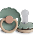 The FRIGG Daisy Silicone Pacifier 2-Pack | Limited Edition by FRIGG features two green scalloped-edge pacifiers with beige ring handles and brown accents—one upright showing the nipple, the other flat displaying the front.