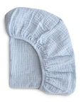The mushie Extra Soft Bassinet Muslin Crib Sheet in light blue is shown partially folded, highlighting its elastic edges and soft, breathable textured fabric—perfect for your baby's bedding.