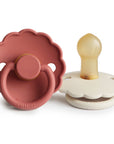 The FRIGG Daisy Natural Rubber Pacifier 2-Pack by FRIGG features one dusty pink pacifier with a daisy-shaped scalloped edge and ring, and one off-white pacifier, both with rounded natural rubber latex nipples for soothing comfort.