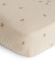 Close-up of mushie's Extra Soft Muslin Crib Sheet in beige, featuring a subtle pattern of small yellow and black bumblebees scattered across the breathable baby bedding.