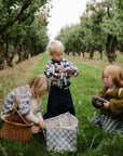 Three kids enjoy fine motor play with mushie’s Silicone Sensory Toy as they gather apples.