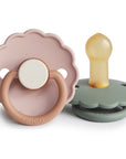 The FRIGG Daisy Natural Rubber Pacifier 2-Pack features two daisy-shaped pacifiers with scalloped edges in light pink, beige, and sage green. Each has a round handle and a natural rubber latex nipple. Brand: FRIGG.