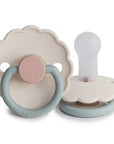 The FRIGG Daisy Silicone Pacifier 2-Pack | Limited Edition by FRIGG features two scalloped-edged pacifiers: one flat with a pastel pink and gray handle, the other upright showing its white, medical-grade silicone nipple for baby comfort.