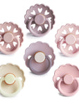 The FRIGG Natural Rubber 6-Pack by FRIGG features six pastel pacifiers in lavender, beige, and pink. Arranged in two rows, the top has heart-cutout edges, the bottom scalloped edges. Made in Denmark with natural rubber latex.