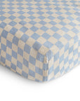 A close-up of the mushie Extra Soft Muslin Crib Sheet, a breathable baby bedding with a blue and white checkered pattern, fitted snugly on a mattress for extra comfort.