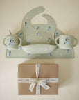 The mushie Bluey Gift Set, featuring a blue dog cartoon silicone bib, cup, and bowl, is displayed on a brown gift box wrapped in white ribbon—a delightful addition to your mushie feeding essentials.