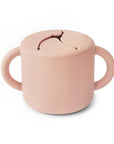 The mushie Snack Cup in Blush is a spill-proof cup with two handles and a flexible lid with slits, allowing easy snack access and preventing spills.